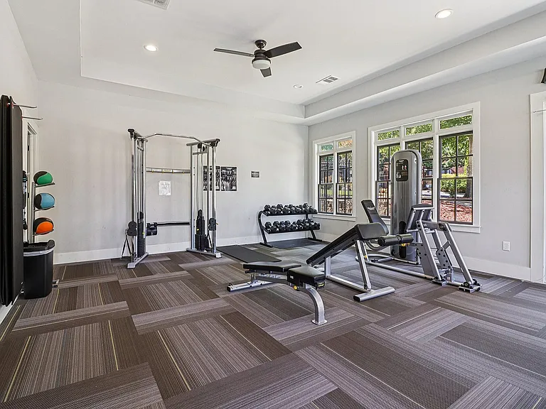 Bright and inviting gym room featuring modern workout equipment, free weights, and large windows letting in natural light.