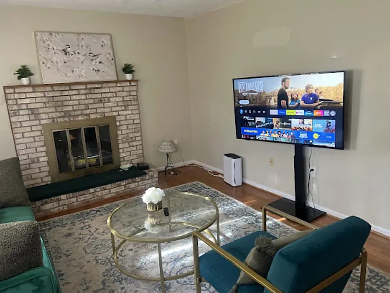Comfortable living room with a brick fireplace, hardwood floors, area rug, and TVideal for relaxing or movie nights.