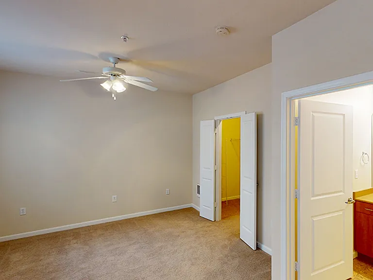 Spacious apartment bedroom with large closet, attached bathroom and plush carpet flooring.