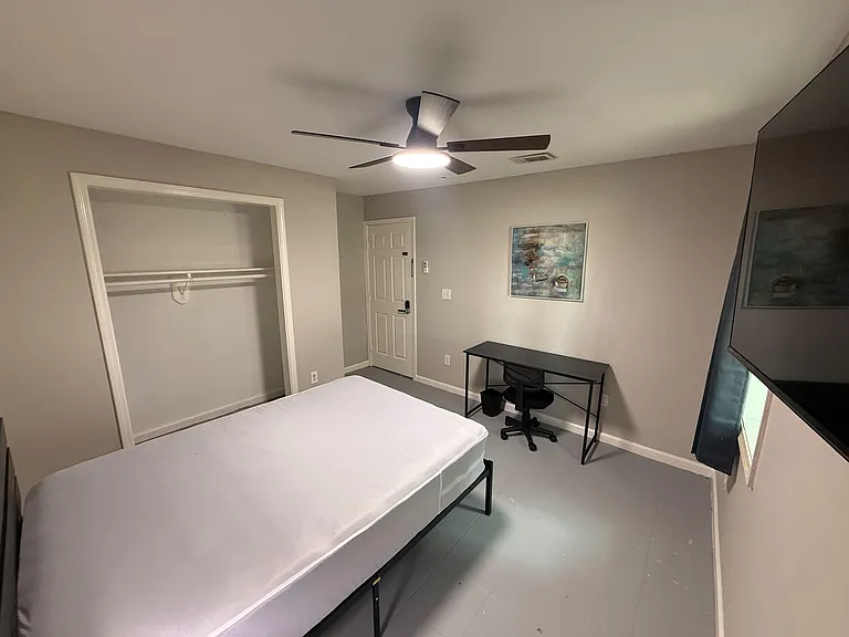 Furnished bedroom with ceiling fan, open closet storage, and a dedicated desk setup near the window for studying.