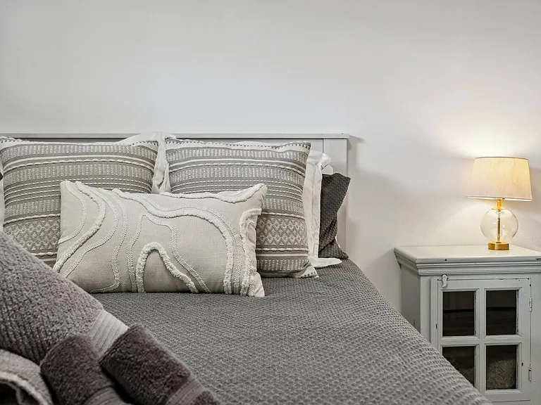 A cozy queen bed with layered pillows and a soft bedside glow_perfect for a relaxing stay.