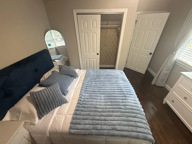 Bedroom features a fully furnished layout with a bed, dresser storage, and a closet, plus window blinds for natural light.