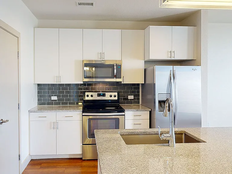 Apartment kitchen with stainless steel appliances, granite countertops and wood-style flooring.