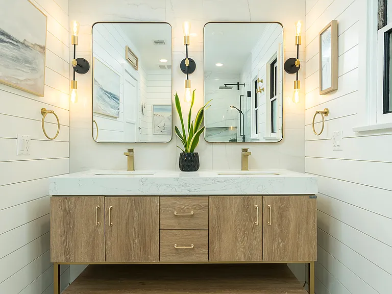 Bright, beautiful bathroom with a spacious glass-enclosed walk-in shower, rainfall and handheld fixtures, a double vanity, designer lighting, shiplap walls, and elegant marble-patterned tile.
