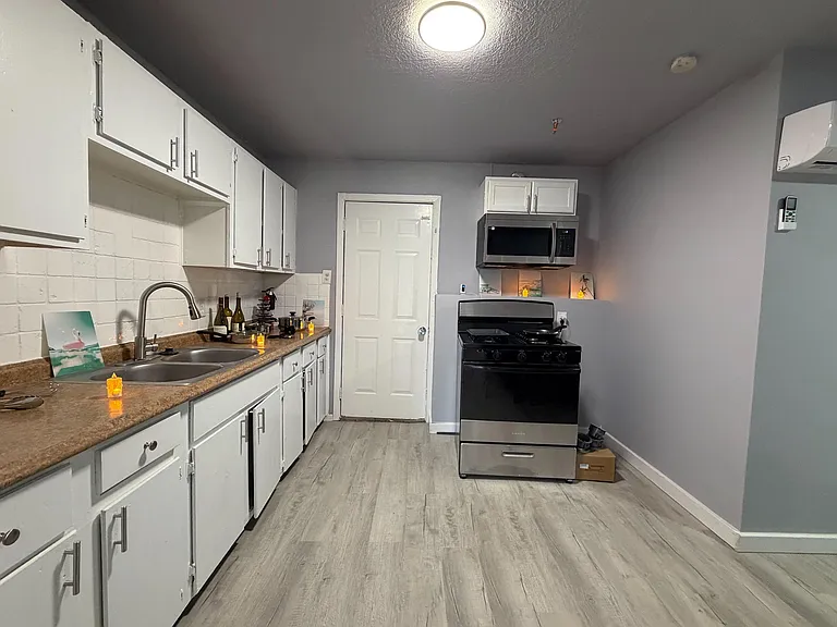 Functional galley kitchen with ample white cabinetry, double-basin sink, and a range with over-the-range microwave.