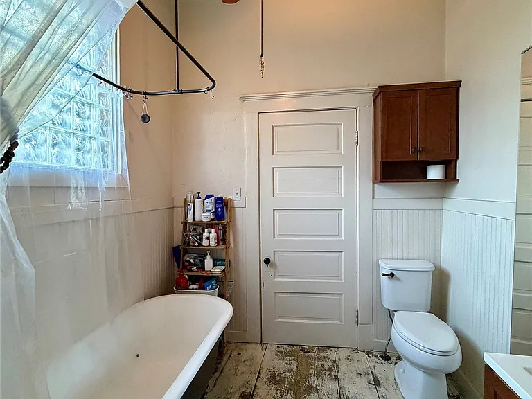 Clawfoot tub with shower curtain rod, a ceiling fan with light fixture, and distressed wood-finish flooring