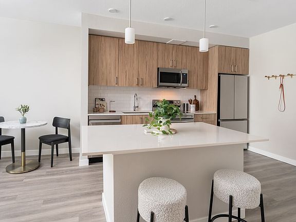 Finish Package II Kitchen with oak cabinetry, white quartz countertops, white tile backsplash, stainless steel appliances, pendant lighting, and hard-surface vinyl plank flooring