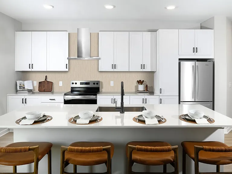 Upgrade Collection Kitchen with white shaker cabinetry, white quartz countertops, over-the-range hood, beige tile backsplash, and stainless steel appliances (Representative photo)