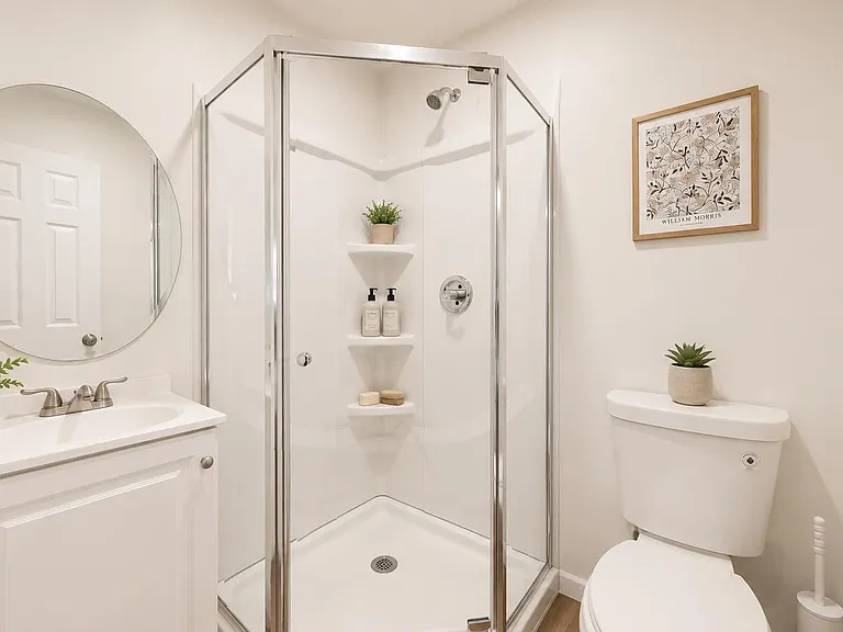 Clean, well-appointed bathroom featuring a glass-enclosed corner shower, vanity with mirror, and neutral finishes.