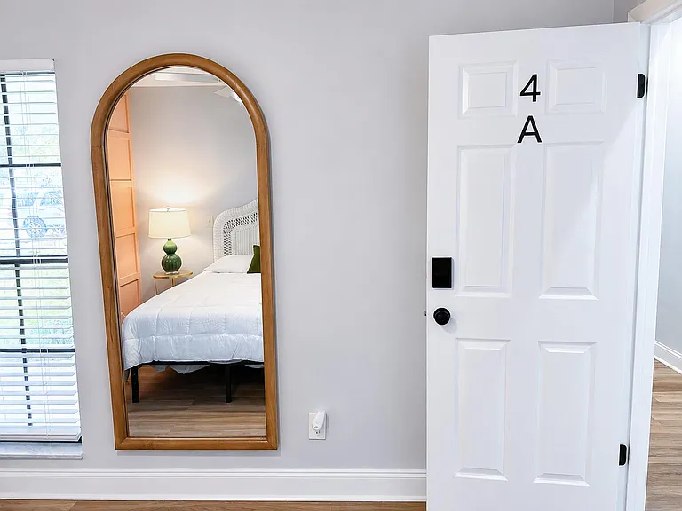 Private bedroom with wood-look flooring, ample wall space, and a window with blinds, furnished with a comfortable bed.