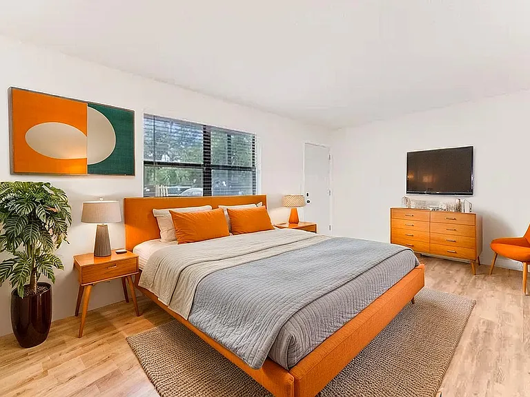 Vibrant bedroom featuring an orange upholstered bed, contemporary furniture, stylish artwork, and a cozy ambiance.