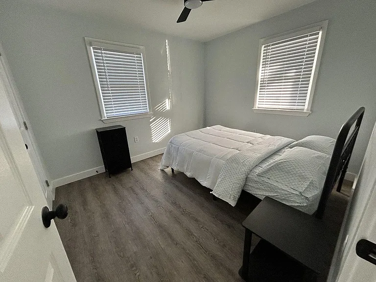 Furnished bedroom featuring a comfortable bed, ceiling fan, and two windows with blinds for adjustable light and privacy.