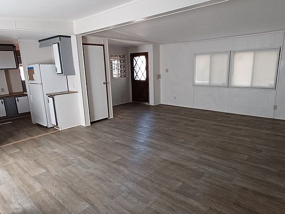 View from the back corner of the living room, looking toward the front door. Showing placement of woodstove and kitchen
