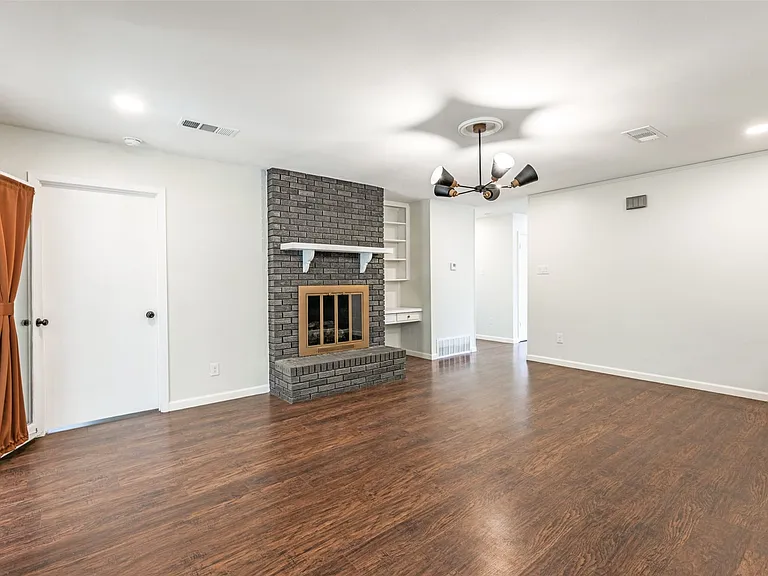 Spacious room featuring wood-finish flooring, a brick fireplace with mantel, recessed lighting, and a modern ceiling fixture
