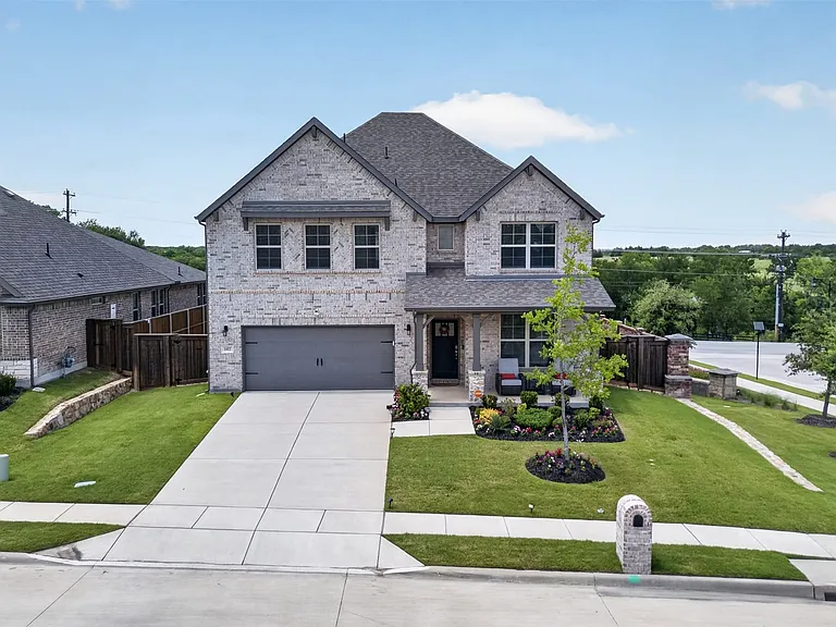 Two-story residence featuring a light-colored brick facade, a dark gray shingled roof, an attached two-car garage, and a concrete driveway