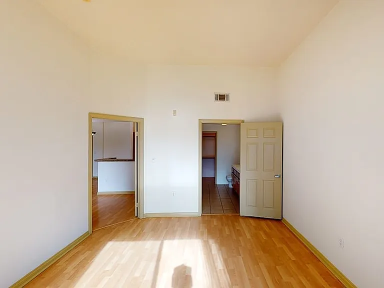 Spacious apartment bedroom with attached bathroom and wood-style flooring.