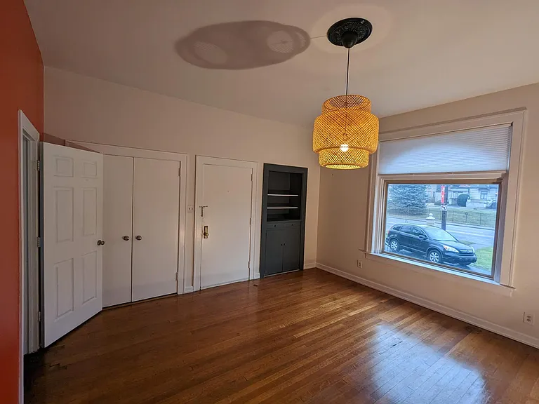 Beautiful front bedroom/dining room with original walnut hardwood floors, a non-functional fireplace, and a large closet and built-in bookshelf.