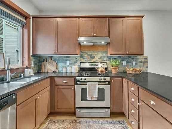 Warm, spacious kitchen featuring granite counters, cherry cabinetry, stainless appliances, and a stylish tile backsplash.
