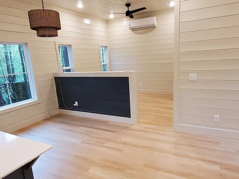 Studio cabin with half-wall room divider from living, dining, and kitchen space. Mini-split HVAC with outdoor compressor.