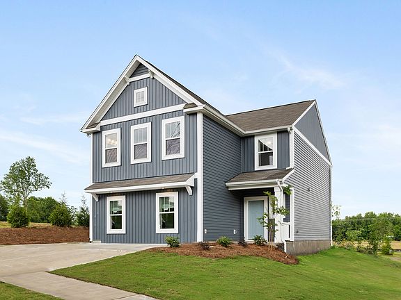 A large gray house with white trim is sitting on top of a lush green field.