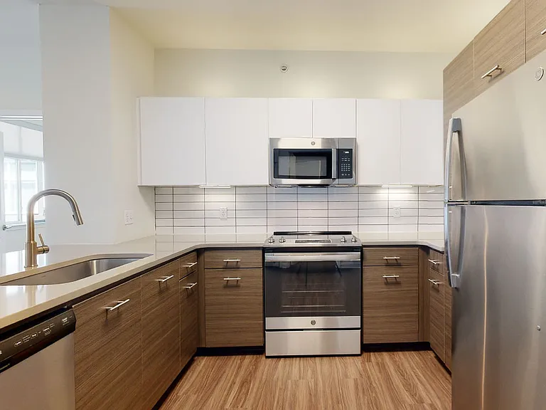 Apartment kitchen with stainless steel appliances, quartz countertops and wood-style flooring.
