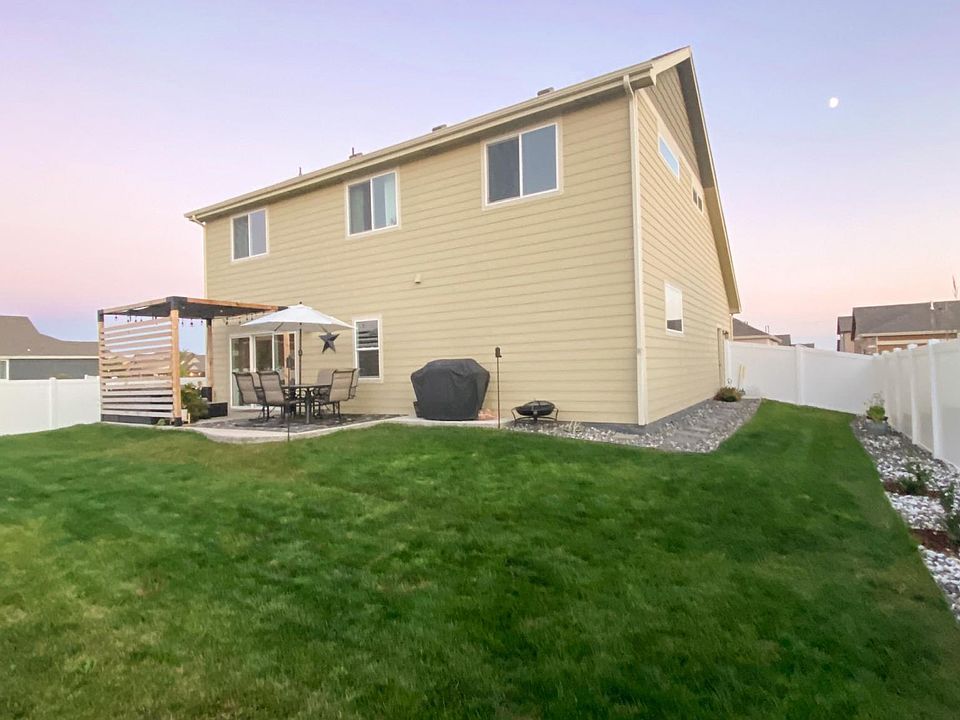 large finished back yard with sprinkler system, multiple trees, shrubs, and an oversized patio with privacy pergola.