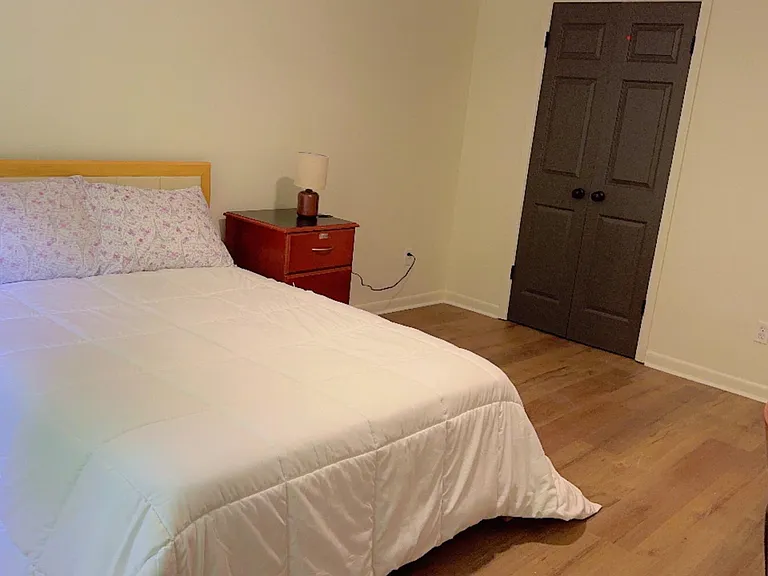 Furnished bedroom with a full-size bed, nightstand with lamp, and double-door closet for convenient storage.