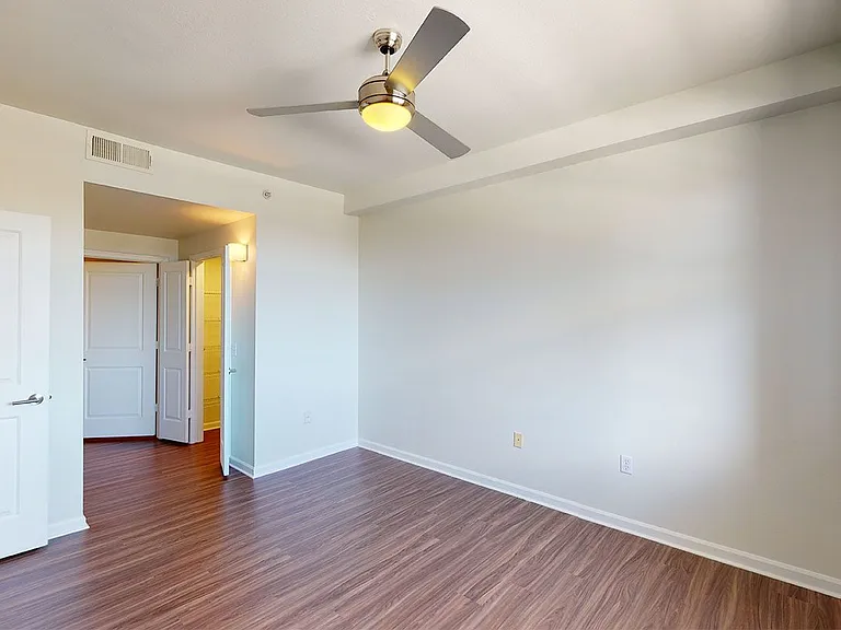 Spacious apartment bedroom with large closet, attached bathroom and wood-style flooring.