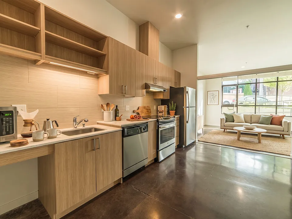 Linear kitchen featuring stainless steel appliances, custom shelving, and polished concrete floors leading into the living room.