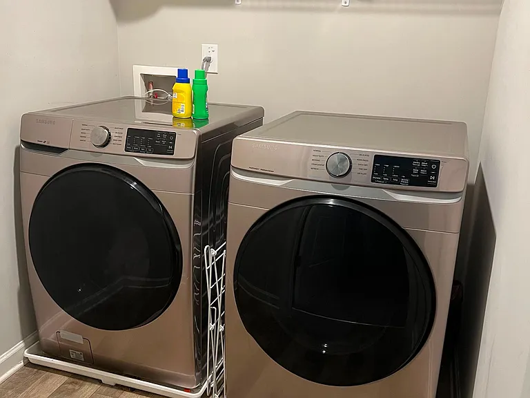 Dedicated laundry area with full-size washer and dryer plus a convenient wire shelf for storing cleaning supplies.