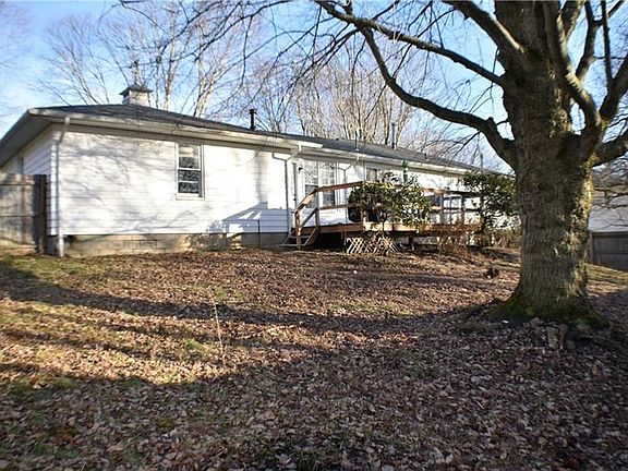 Back of home showing fenced in yard, shade tree, and wooden deck.