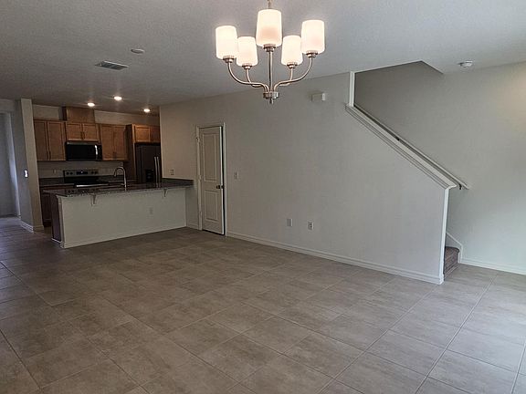 Wide view of the open-concept living and dining area showcasing tile flooring, staircase access, and seamless flow to the kitchen.