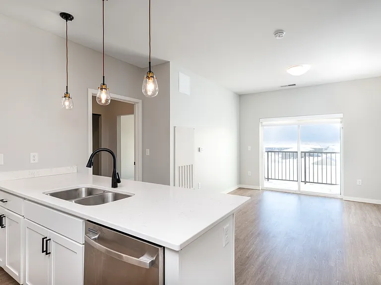 Bright modern kitchen with sleek white countertops, stylish pendant lighting, and open-concept living area leading to a balcony with scenic views. Bright modern kitchen with sleek white countertops, stylish pendant lighting, and open-concept living area l