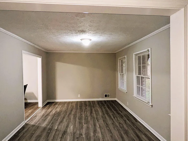 Open living area with durable wood-look flooring, crown molding, and multiple windows with blinds for natural light.