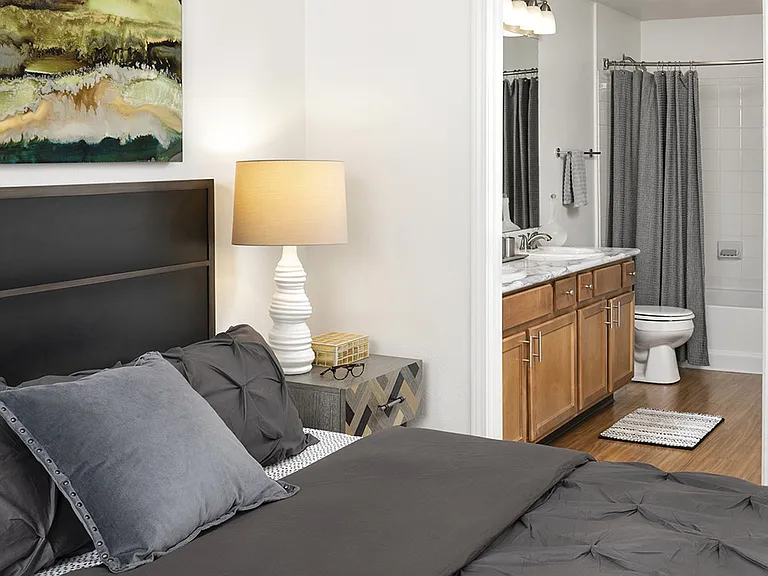Spacious apartment bedroom with wood floors overlooking bathroom.