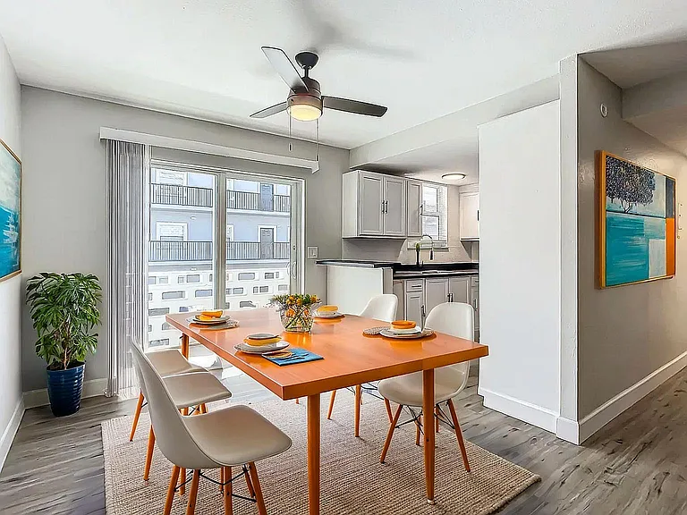 Chic dining area with modern orange table, sleek white chairs, and vibrant artwork in a sunlit apartment setting.