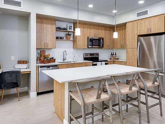 Open concept kitchen with quartz countertop, island, stainless steel appliances, tile backsplash and work from home nook