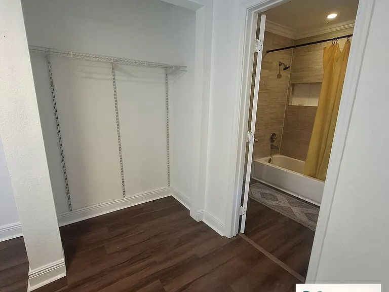 Private en-suite bathroom with tub/shower combo and tiled surround, plus an adjacent closet with built-in shelving.