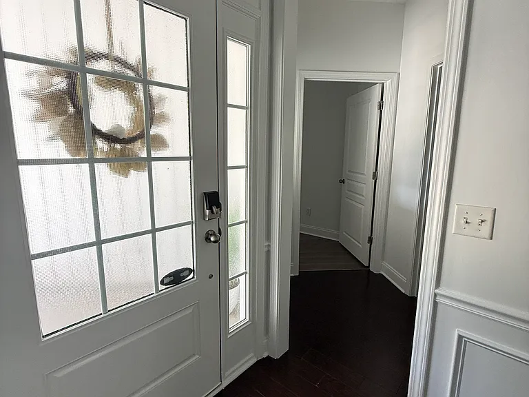 A welcoming first impression! Elegant front entry foyer featuring crisp wainscoting wall paneling, rich dark hardwood floors, and a secure smart-lock front door framed by stylish glass sidelights."