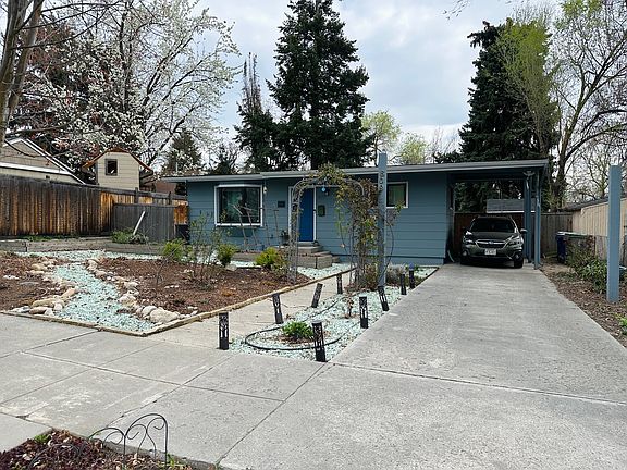 Front of the house with four raised beds. Includes carport and driveway. Can fit three cars