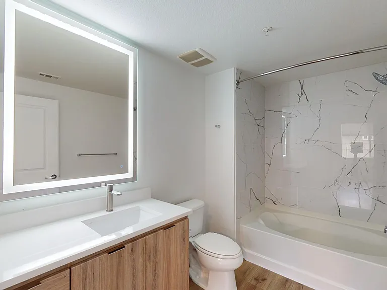 Apartment bathroom with large soaking tub, LED vanity mirror, and wood style floor.