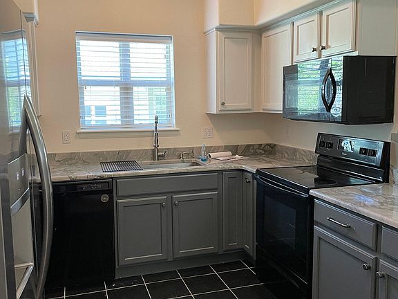 Quartz counters in kitchen with dishwasher, refrigerator, stove, and microwave.