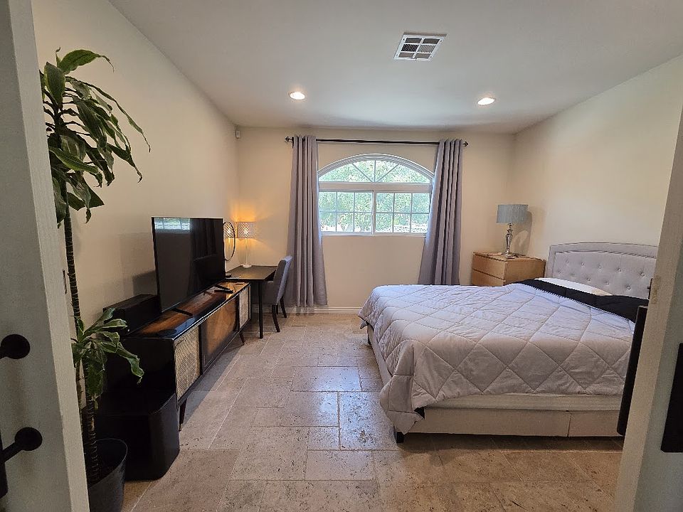 Furnished bedroom with queen bed, desk, high ceilings.