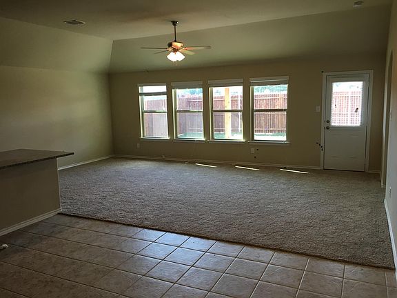 Large Great Room with ceiling fan and four large windows (plus fifth in door) looking out over covered patio and enclosed back yard