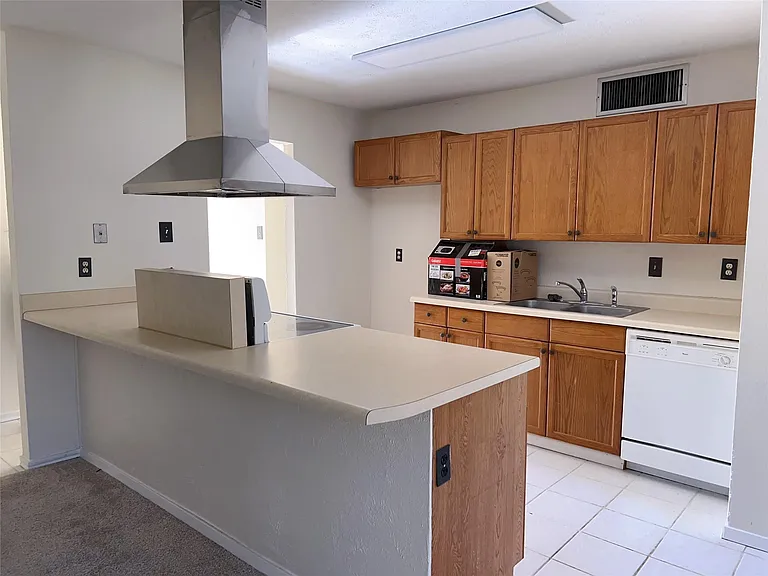 Kitchen featuring kitchen peninsula, dishwasher, island range hood, sink, and light tile floors