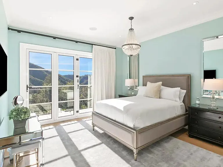 Guest bedroom with a King Bed accented with an elegant chandelier and views of Beverly Hills, hillside.