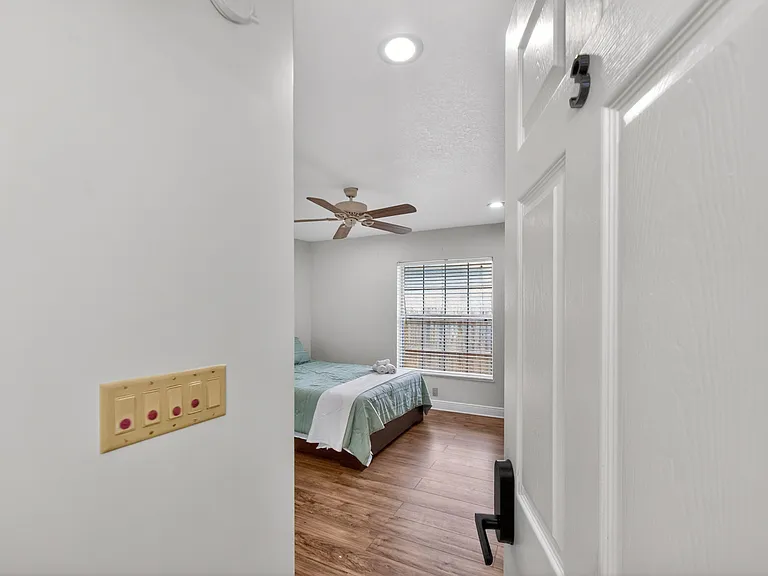 Private bedroom with wood-look floors, ceiling fan, and a large window with blinds for natural light and privacy.