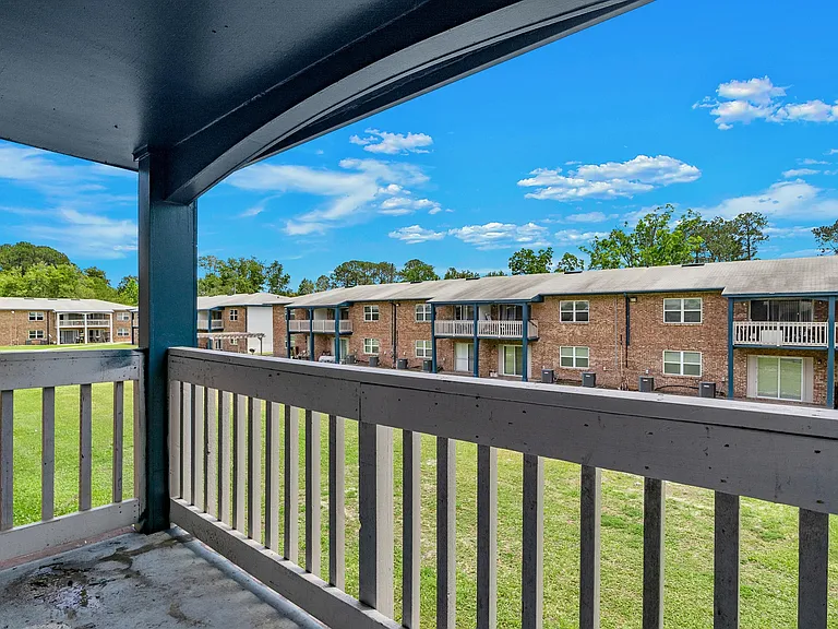 Charming apartment balcony view showcasing lovely brick buildings, lush green lawns, and a bright blue sky.