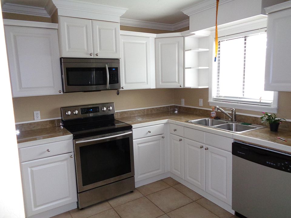 White cabinets with crown on wall cabinets as well as crown on kitchen walls. Custom wood-look tile countertops with marble trim. New white appliances soon to be installed. Custom tile floors. Custom light over new stainless steel sink with new faucet.