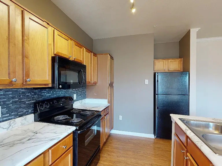 Apartment kitchen with marble-style countertops and wood-style flooring.
